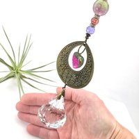 With a nod to bright tones and textures, this one of a kind large crystal sun catcher hanging, holds a gorgeous shape and design featuring a 60mm faceted crystal prism (epic rainbow maker) with unique gemstones. An exceptional piece and quite lovely when hung.  Finished with a sturdy chain and solid  hook for easy hanging.
