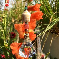 This charming handmade crystal hanging will adorn any room with rainbows and lively reflections, making it a delightful addition for yourself or a thoughtful gift that will be treasured.Featuring a high-quality, medium (40mm) faceted crystal prism, meticulously hand-strung with Howlite gemstone Buddha Focal, Cherry Quartz and distinctive Czech glass beads. It is completed with chain and hook, ensuring effortless hanging and allowing gentle movement that makes the rainbows dance.