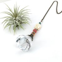 This charming handmade crystal hanging will adorn any room with rainbows and lively reflections, making it a delightful addition for yourself or a thoughtful gift that will be treasured.Featuring a high-quality, medium (40mm) faceted crystal prism, meticulously hand-strung with Howlite gemstone Buddha Focal, Cherry Quartz and distinctive Czech glass beads. It is completed with chain and hook, ensuring effortless hanging and allowing gentle movement that makes the rainbows dance.