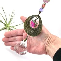 With a nod to bright tones and textures, this one of a kind large crystal sun catcher hanging, holds a gorgeous shape and design featuring a 60mm faceted crystal prism (epic rainbow maker) with unique gemstones. An exceptional piece and quite lovely when hung.  Finished with a sturdy chain and solid  hook for easy hanging.