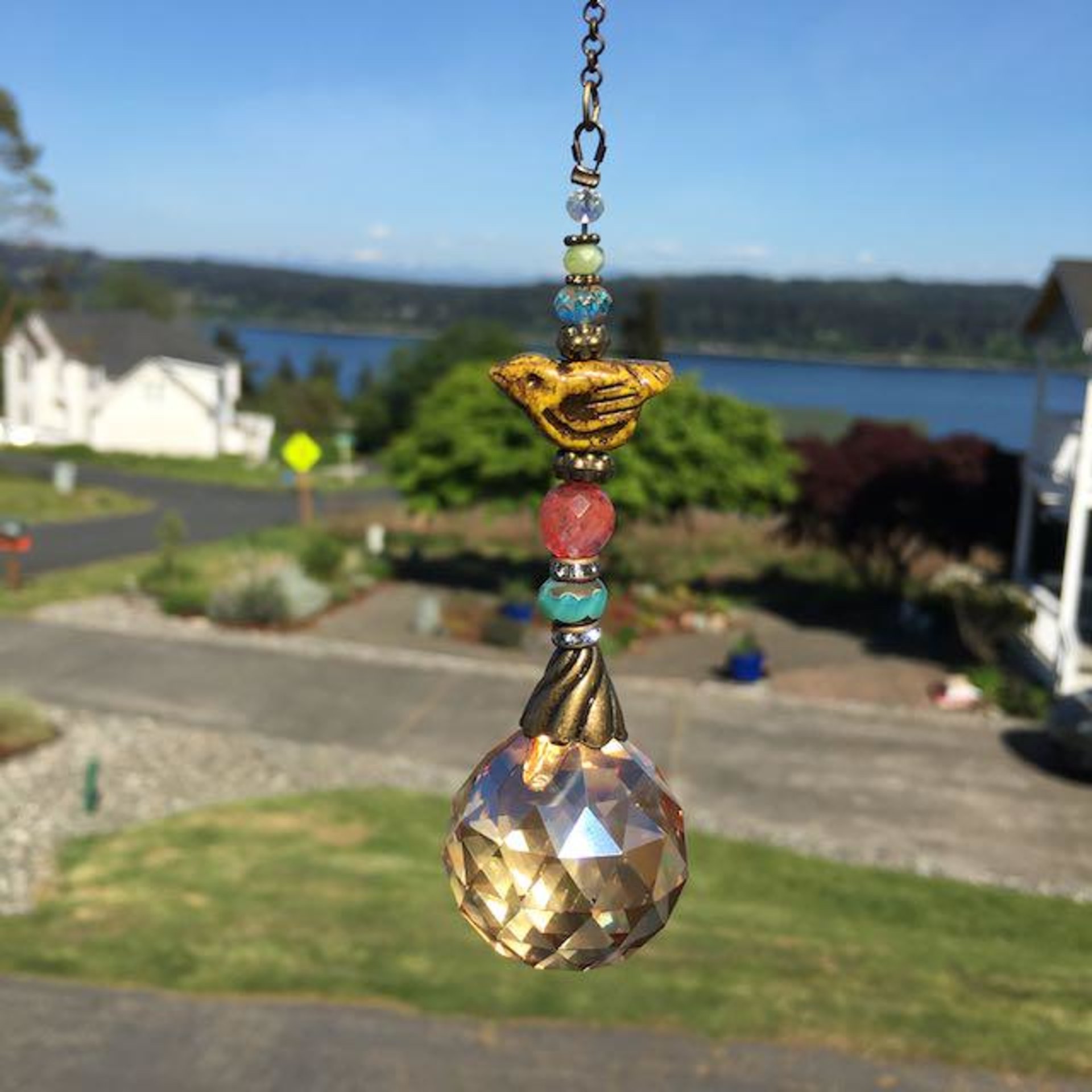 This charming handmade crystal sun catcher hanging will adorn any room with rainbows and bring lively reflections. Simple and elegant, our unique design features a high-quality Asfour Honey AB (30mm) faceted crystal prism sphere, meticulously hand-strung with unique beads. Czech Glass bird focal, vintage Czech Glass beads and Cherry Quartz gemstone. It is completed with chain and hook, ensuring effortless hanging and allowing gentle movement that makes the rainbows dance. Hanging Length of 17".