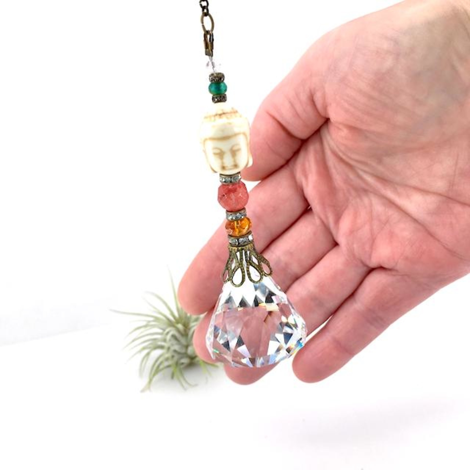 This charming handmade crystal hanging will adorn any room with rainbows and lively reflections, making it a delightful addition for yourself or a thoughtful gift that will be treasured.Featuring a high-quality, medium (40mm) faceted crystal prism, meticulously hand-strung with Howlite gemstone Buddha Focal, Cherry Quartz and distinctive Czech glass beads. It is completed with chain and hook, ensuring effortless hanging and allowing gentle movement that makes the rainbows dance.