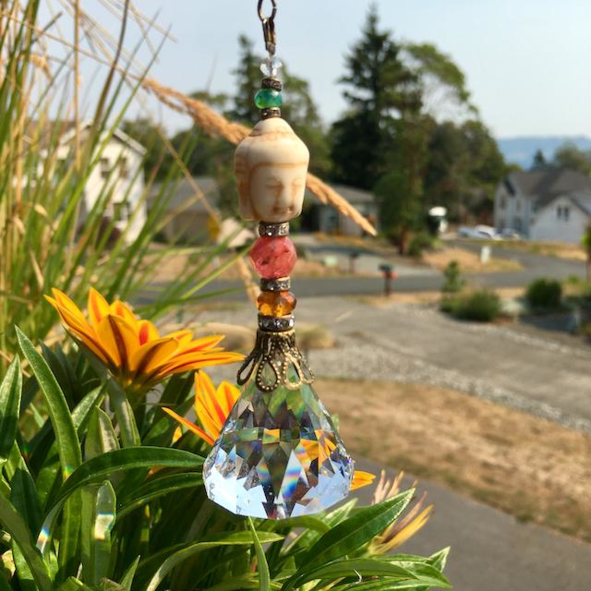 This charming handmade crystal hanging will adorn any room with rainbows and lively reflections, making it a delightful addition for yourself or a thoughtful gift that will be treasured.Featuring a high-quality, medium (40mm) faceted crystal prism, meticulously hand-strung with Howlite gemstone Buddha Focal, Cherry Quartz and distinctive Czech glass beads. It is completed with chain and hook, ensuring effortless hanging and allowing gentle movement that makes the rainbows dance.