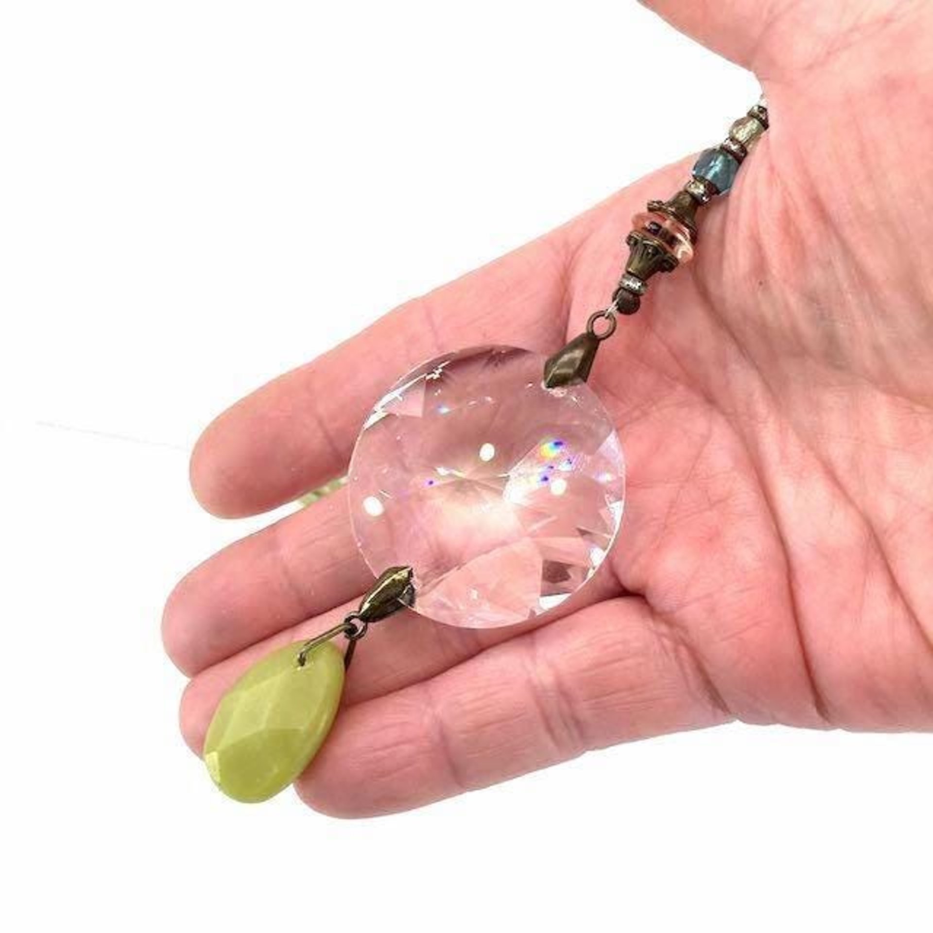 This charming bohemian inspired crystal sun catcher hanging with Jade gemstone drop is a minimalist style hanging. The prism focal is a high-quality Asfour 40mm crystal, renowned for casting rainbows and reflections that dance across the room. Beautiful faceted Jade gemstone drop, thoughtfully strung together with vintage Czech glass beadsand finished with a versatile chain for easy hanging in a variety of spaces, from your car's rearview mirror to a cozy corner of your home.