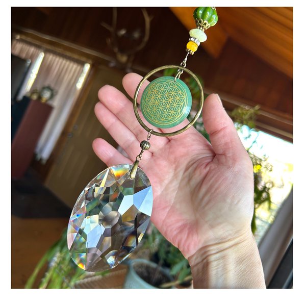 With a nod to natural tones and textures, this one of a kind large crystal sun catcher hanging, holds a gorgeous shape and design featuring a very large 110mm crystal prism (2.5 x 3.5 inches) with unique Flower of Life pattern carved on a beautiful Aventurine stone. Various gemstones and beads.  An exceptional piece and quite lovely when hung.  Exceptional rainbows!